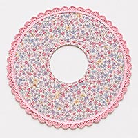 Instructional doll-making image showing pink scalloped lace and narrow satin ribbon attached around the outside edge of a floral fabric circle, demonstrating the correct placement of the lace trim for a doll pin dress skirt.